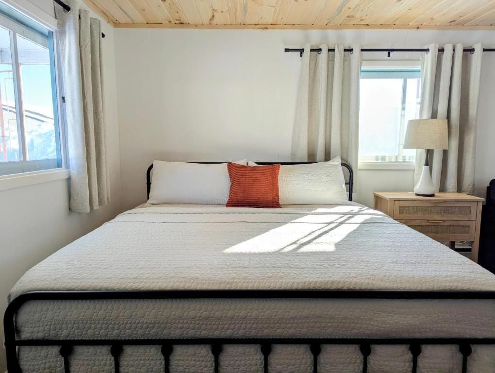 Un dormitorio con cama, cortinas, mesita de noche y lámpara.