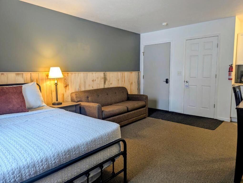 Una habitación de hotel con cama, sofá, lámpara y puerta.