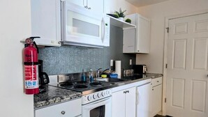Une cuisine avec des meubles blancs, un four à micro-ondes, une cuisinière et un extincteur.