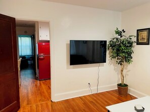 A room with a flat-screen TV mounted on the wall, a wooden floor, a red refrigerator, and a potted plant. - Terrific 2 units: Side-by-Side 1-Bedroom Duplex Apt... near Airport, Downtown (Charlotte)