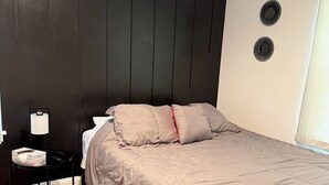 Un dormitorio con cama, mesita de noche, lámpara y aire acondicionado instalado en la pared.
