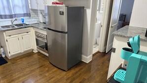 Una cocina moderna con armarios blancos, un refrigerador de acero inoxidable, horno empotrado, pileta y una cafetera color verde azulado sobre una encimera negra.