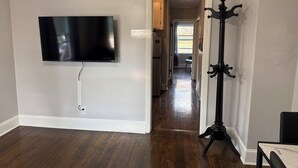 Habitación con televisor de pantalla plana en la pared, perchero y suelo de madera.