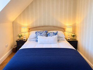 Een slaapkamer met een groot bed, twee nachtkastjes met lampen en een schuine plafond.