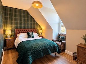 Ein Schlafzimmer mit einem großen Bett, einem Sessel, einem Nachttisch, einer Lampe und einem Fenster.