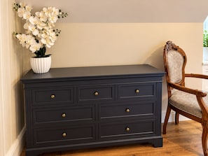 A dark wooden dresser with brass knobs, a white vase with white flowers, and a wooden chair with a cushioned seat. - Central Ayr Attic Apartment + Panoramic Town Views (Ayr)