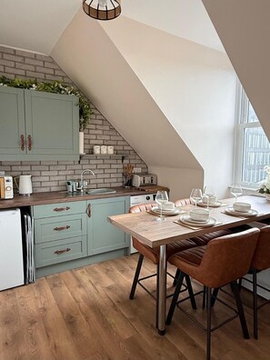 A modern kitchen with a dining area, featuring a brick wall, light blue cabinets, and a wooden dining table with leather chairs.