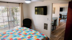 Um quarto com uma cama, uma cadeira, uma televisão e uma janela com persianas.