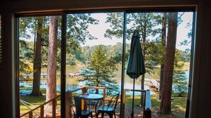 Um deck de madeira com mesa e cadeiras, com vista para um lago com árvores e um píer.