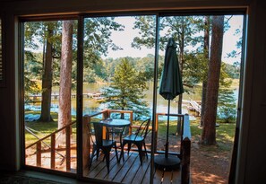 A wooden deck with a table and chairs, overlooking a lake with trees and a dock. - New Listing! Waterfront Toledo Bend Lake House w/ Private Dock - Sleeps 6 (Many)