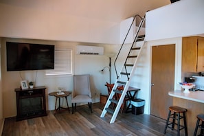 A compact living space with a TV, a small table with a plant, a chair, a staircase, and a kitchen area with stools. - New Listing! Waterfront Toledo Bend Lake House w/ Private Dock - Sleeps 6 (Many)