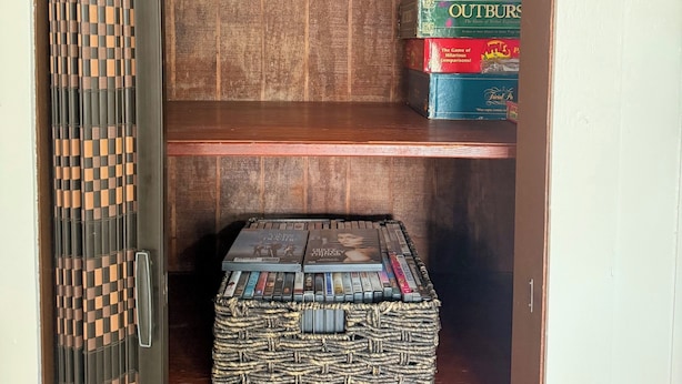 Um armário de madeira com prateleiras contendo livros, uma cesta de palha e dois almofadas vermelhas.