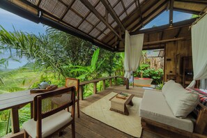 Una terraza de madera con un sofá, una mesa y un banco, con vistas a exuberante vegetación.