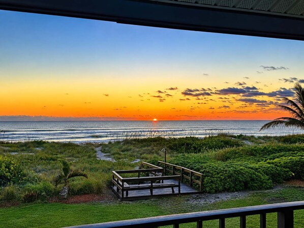 A sunset view from a covered deck with a wooden walkway leading to a bench area. - Oceanfront Quiet Beach + Rocket Launches (Cocoa Beach)