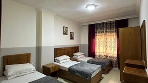 Une chambre d’hôtel avec trois lits, une armoire en bois et une petite table.