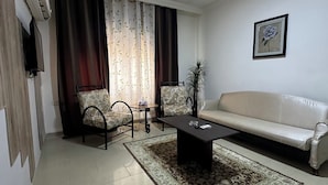 Un salon comprenant un canapé, deux fauteuils, une table basse, un tapis et un téléviseur fixé au mur.