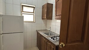 Une cuisine compacte avec des murs recouverts de carreaux blancs, un évier encastré, des placards en bois et un réfrigérateur blanc.