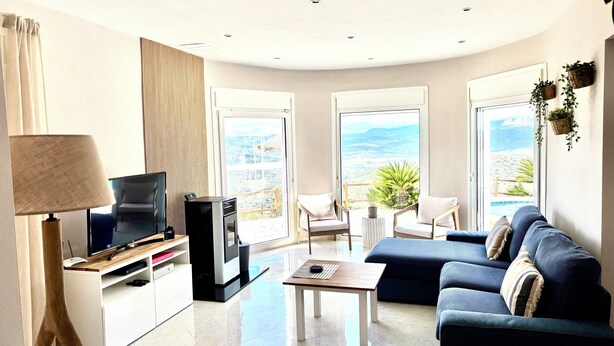 Ein modernes Wohnzimmer mit Flachbildfernseher, einer Couch, einem Couchtisch und einem Balkon mit Blick auf den Strand.