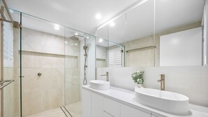 A modern bathroom with a glass-enclosed shower, two white sinks, and a large mirror. - Rare 4BR Ground Floor Exclusive Apt (Mooloolaba)