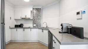 A modern kitchen with white cabinets, a black and white backsplash, a built-in dishwasher, and a coffee machine. - Rare 4BR Ground Floor Exclusive Apt (Mooloolaba)