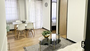 Une pièce moderne et bien éclairée, comprenant un coin repas, une table basse en verre ornée d’une plante et un grand miroir qui reflète l’ensemble de la pièce.