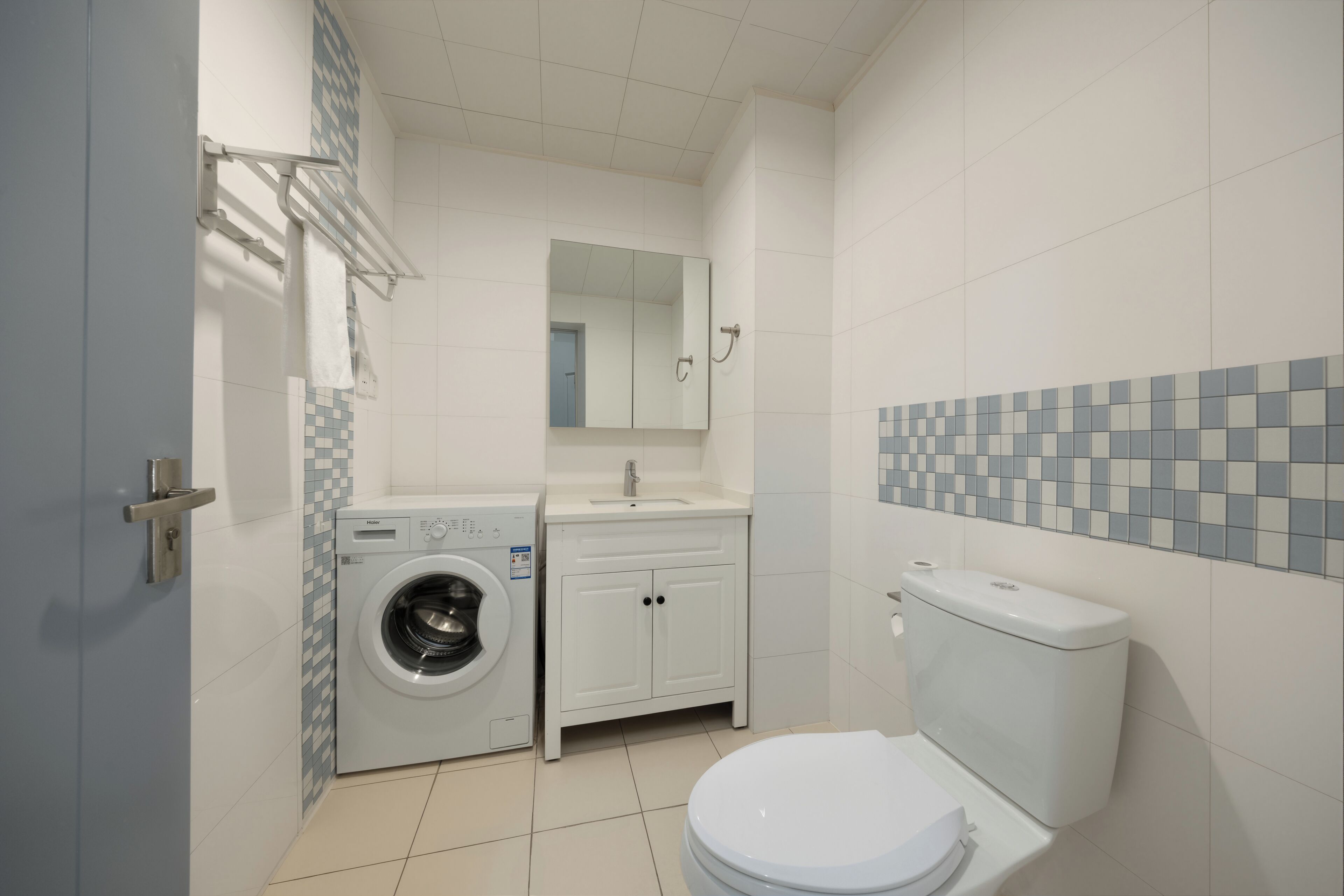 A compact bathroom with a washing machine, a toilet, a sink, and a mirror.