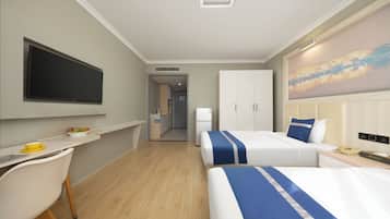 Habitación de hotel con televisión de pantalla plana, dos camas con ropa de cama azul y blanca, un escritorio con silla, un cuadro en la pared y vistas al área de la cocina.
