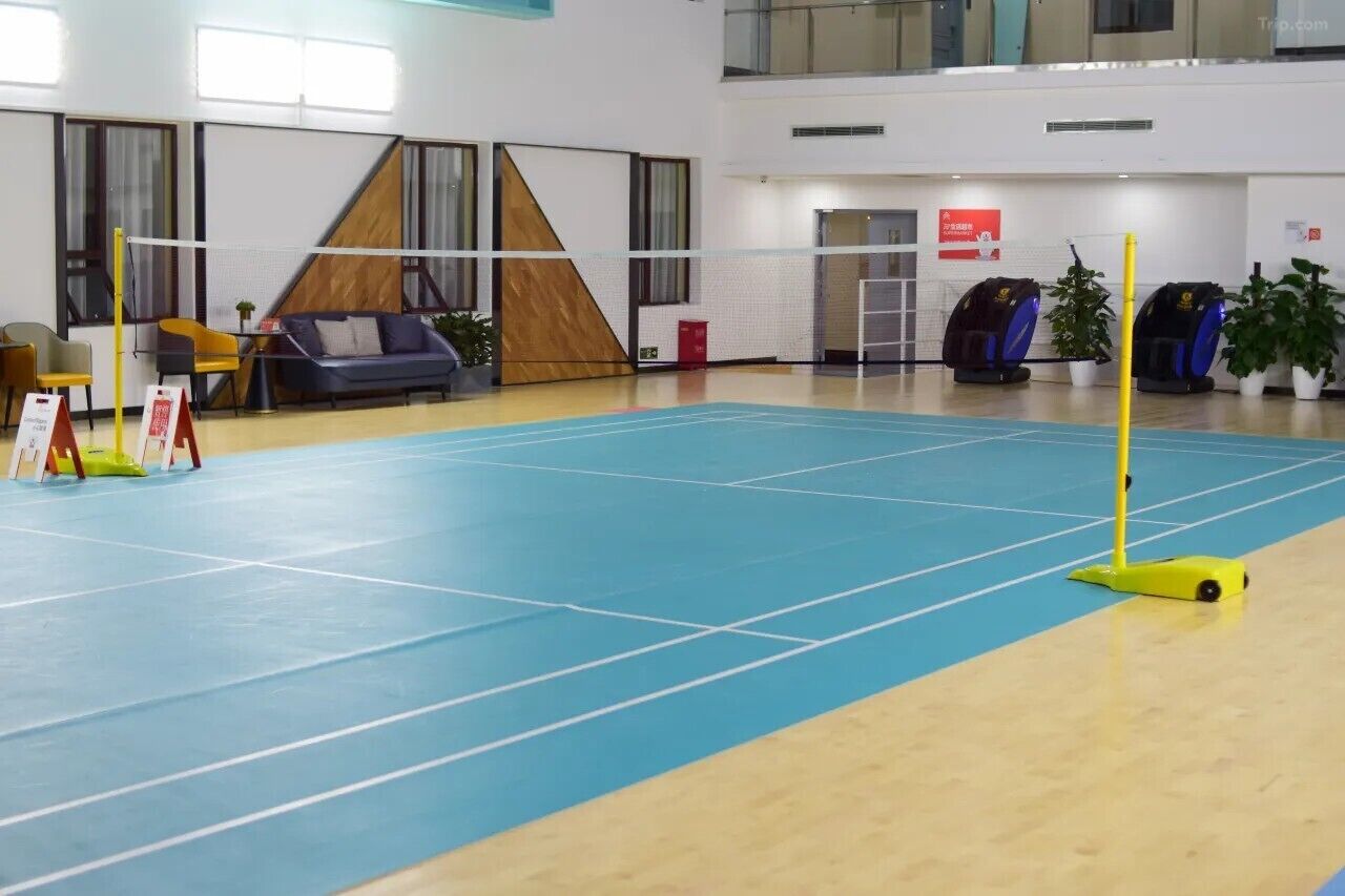 An indoor sports hall with a volleyball net, seating area, and exercise equipment.