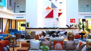 A modern hotel lobby with a central reception desk, multiple seating areas with sofas and chairs, and a decorative wall with geometric shapes. - Golden Phoenix PEK Airport T3 Beijing (Beijing)
