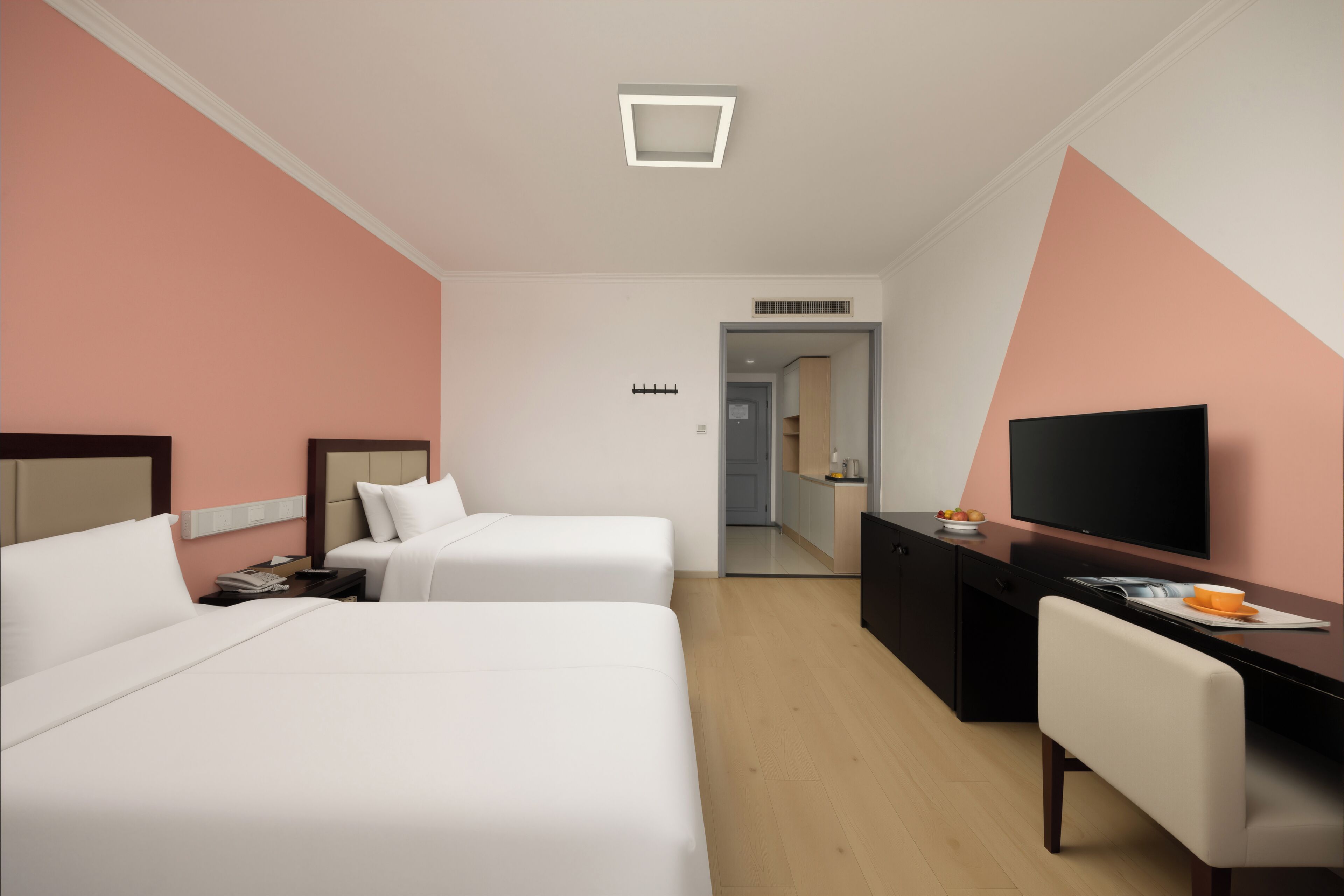 A hotel room with two beds, a desk, a television, and a mirror.