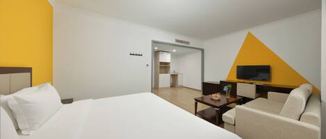 A hotel room with a bed, a sofa, a TV, a small table, and a kitchenette.
