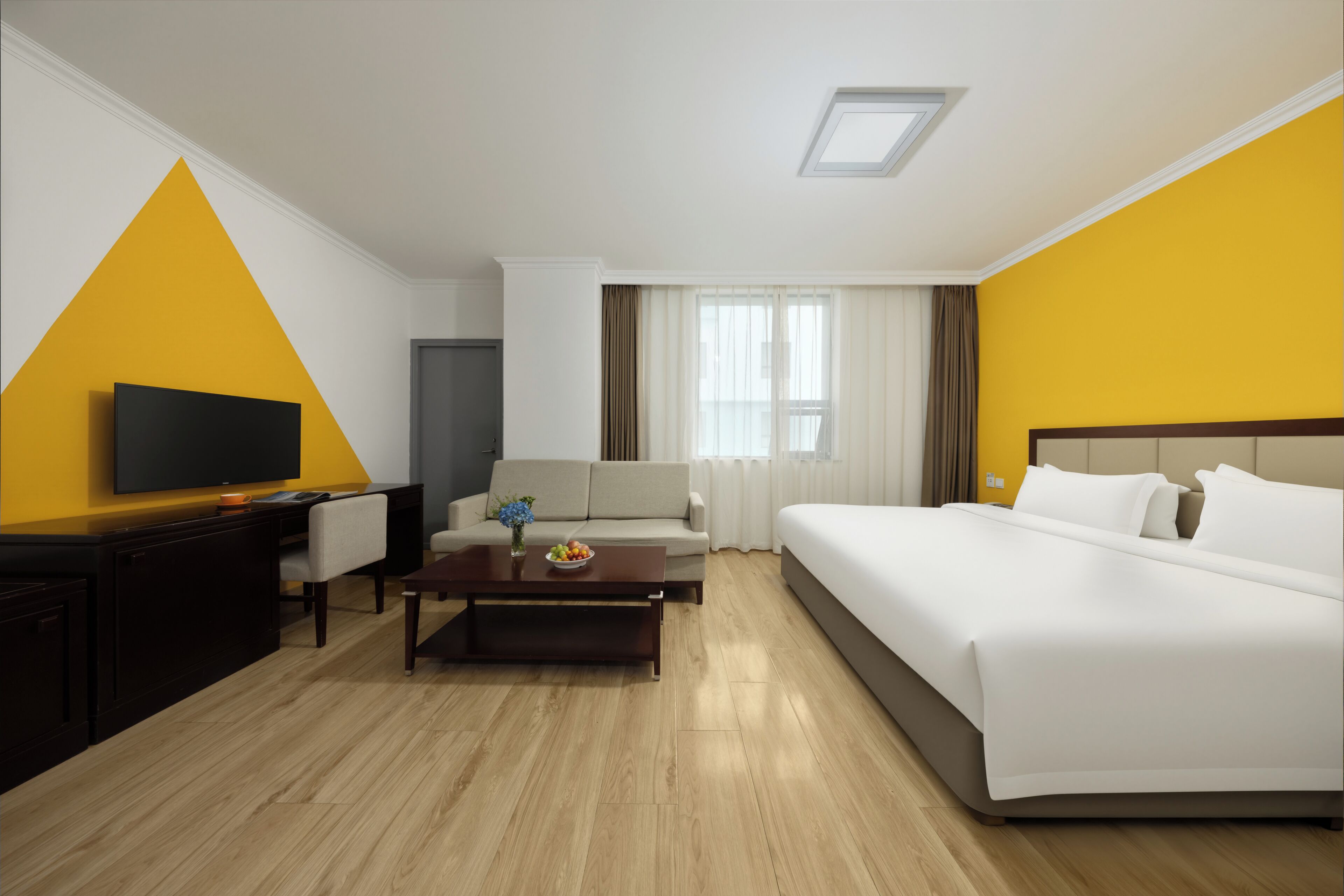 A hotel room with a bed, a television, a sofa, a coffee table, and a desk.
