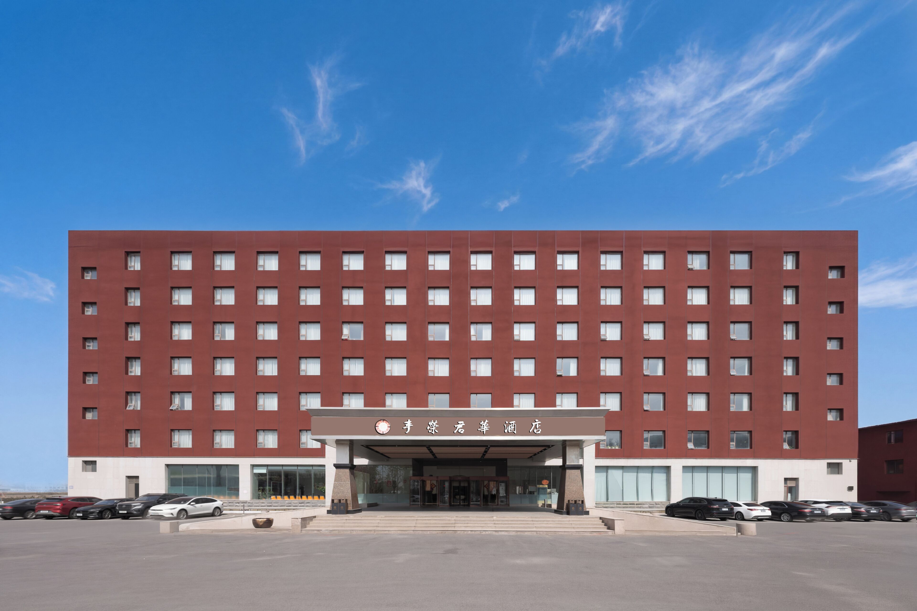 A multi-story hotel with a red facade, large windows, and a parking lot in front.