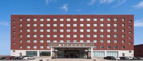 A multi-story hotel with a red facade, large windows, and a parking lot in front.