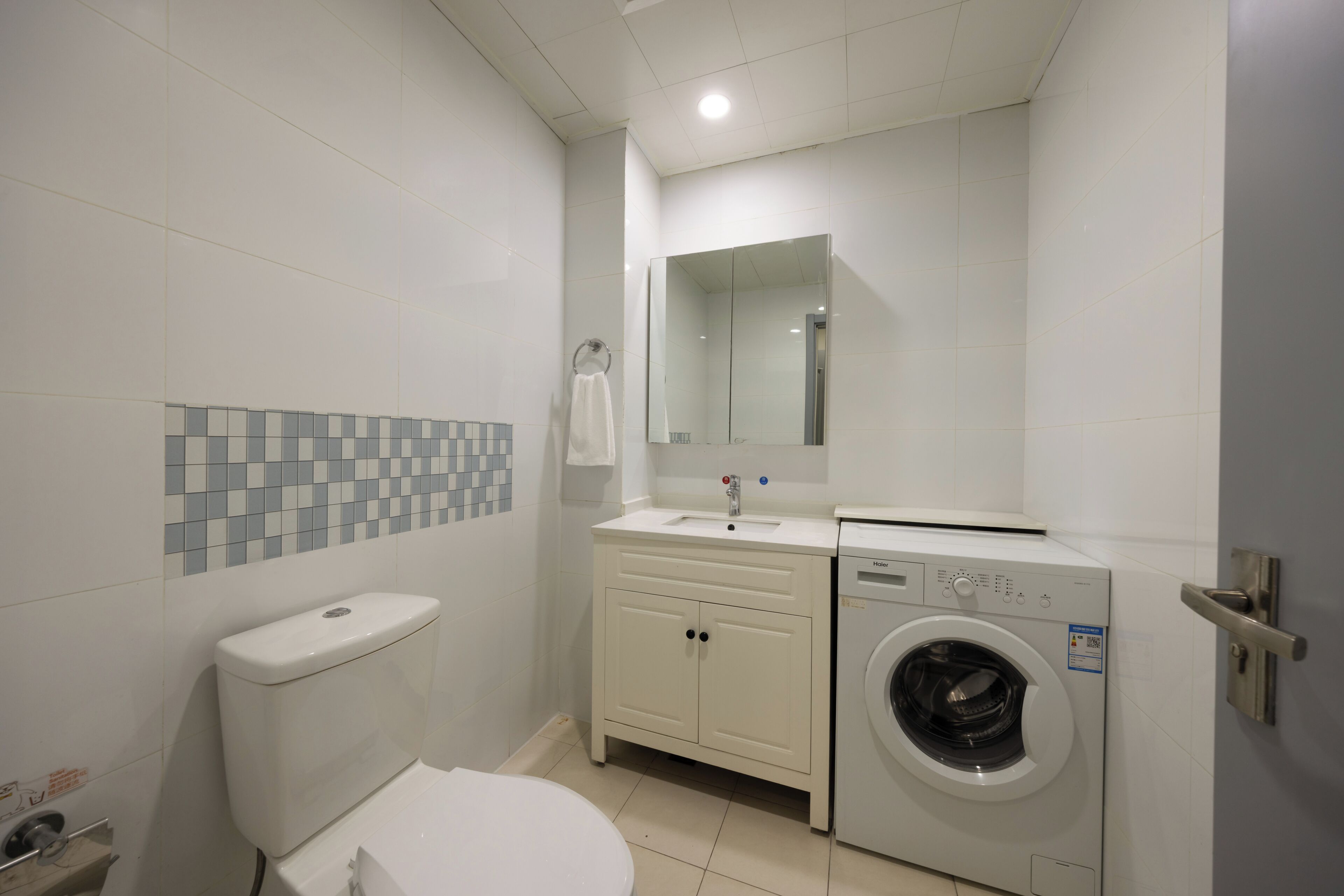 Badeværelse med toilet, håndvask, spejl og vaskemaskine.