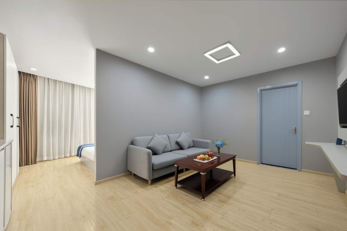A modern living room with a grey sofa, a wooden coffee table with fruit, recessed ceiling lights, and a blue door.