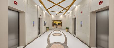 A modern hallway with elevators, numbered doors, and a central decorative floor pattern.