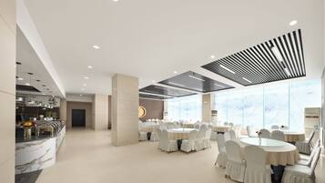 A modern hotel lobby with round tables, white chairs, a marble reception desk, and large windows.