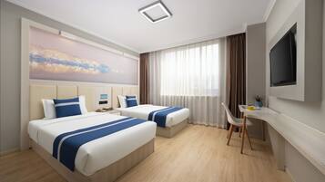 Habitació d'hotel amb dos llits, un escriptori, una televisió i una finestra gran amb cortines.
