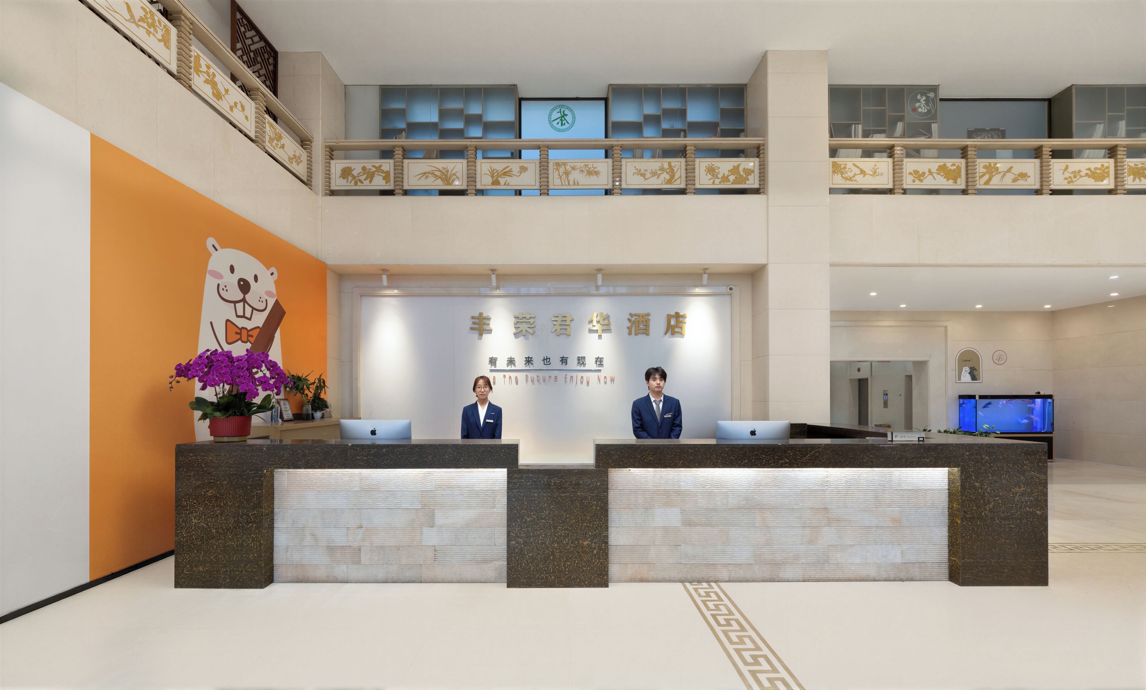 A hotel reception desk with a large bear decoration, two receptionists, and a digital screen above.