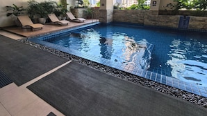 An indoor pool with lounge chairs and potted plants, surrounded by high-rise buildings. - Isla Room by Lakbay Urban Living (Makati)