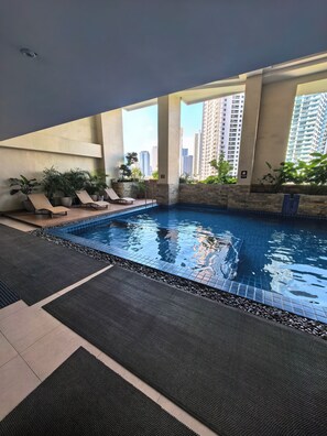 An indoor pool with lounge chairs and potted plants, surrounded by high-rise buildings. - Isla Room by Lakbay Urban Living (Makati)