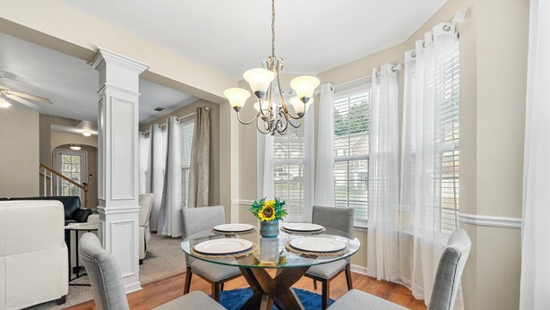 Un coin repas comprenant une table en verre, quatre chaises, un lustre et un vase rempli de fleurs.