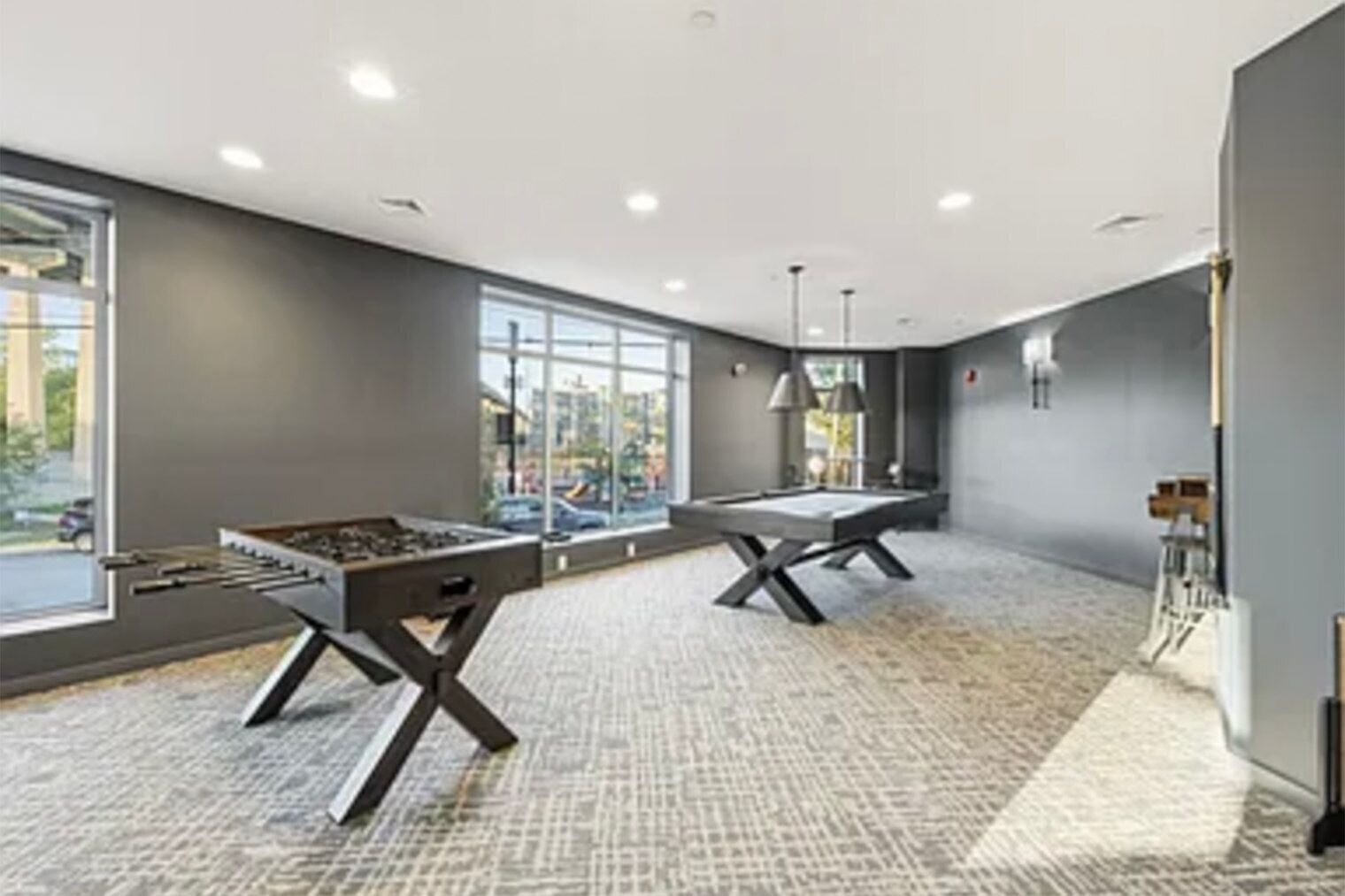 A modern room with two foosball tables, large windows, and a carpeted floor.