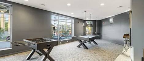 A modern room with two foosball tables, large windows, and a carpeted floor.