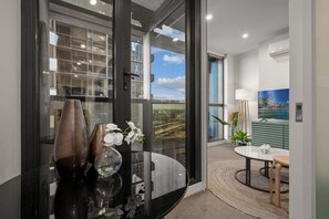 Ein modernes Interieur mit einer Glastür, die auf einen Balkon führt, einem runden Tisch und einer Vase mit Blumen.