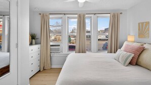 Quarto com uma cama grande, um ventilador de teto e vista para o exterior através de várias janelas.