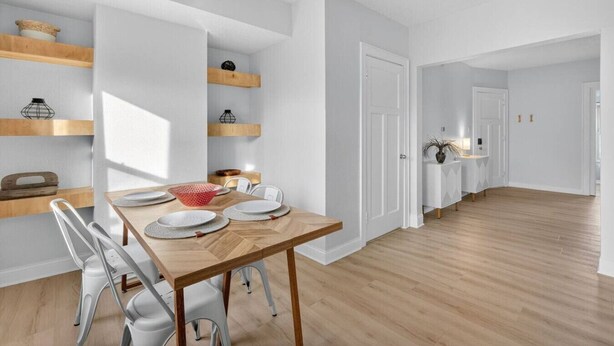 Uma sala de jantar moderna com uma mesa de madeira, cadeiras brancas e estantes embutidas com objetos decorativos.
