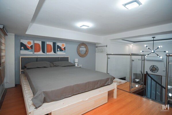 A modern bedroom with a bed, artwork on the wall, and a staircase with glass railings. - Woodlands Condotel (Bulan)