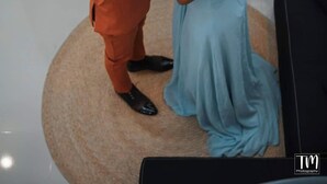 A man and a woman in formal attire standing on a circular rug in a room with a wooden door, a small table with a potted plant, and a window with blinds. - Woodlands Condotel (Bulan)